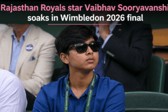 Teenage Indian cricketer Vaibhav Sooryavanshi dressed in a formal black blazer, striped tie, and sunglasses while attending the Wimbledon tennis tournament.
