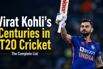 Virat Kohli wearing his blue India jersey celebrating on the field with a teammate, looking up with his helmet removed and bat raised.
